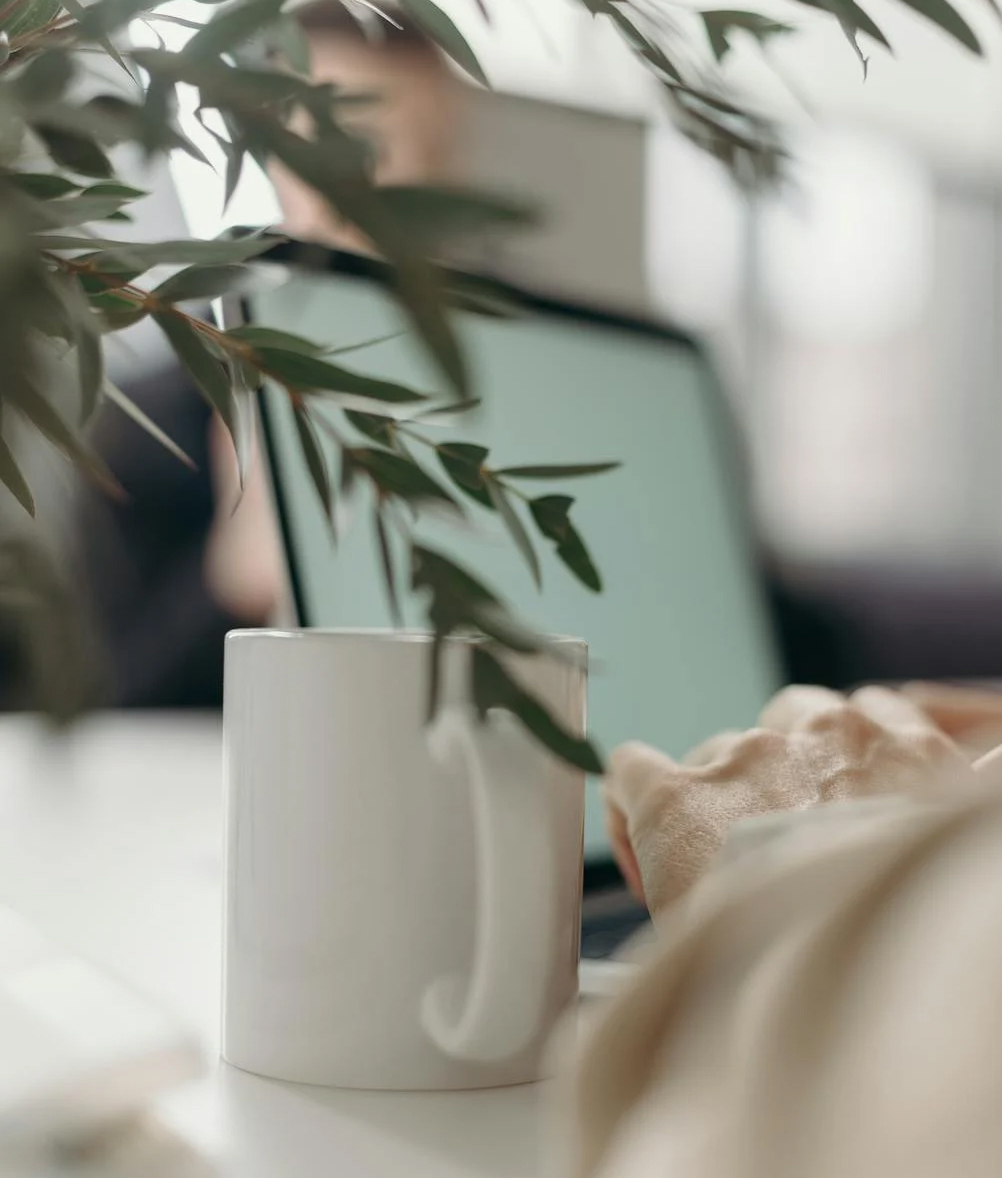 close up of woman typing on laptop with coffee cup and plant branches in the foreground